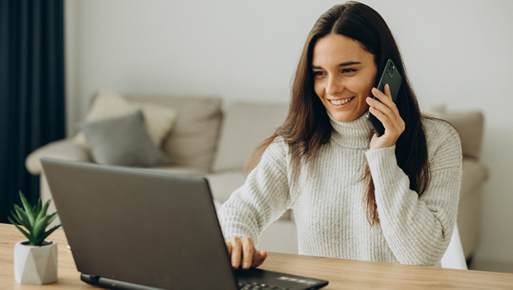 Mujer Atendiendo Llamada Mujer sonriente hablando por teléfono mientras usa un computador portátil en casa