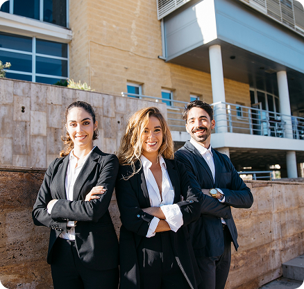Tres profesionales sonrientes con los brazos cruzados frente a un edificio moderno.